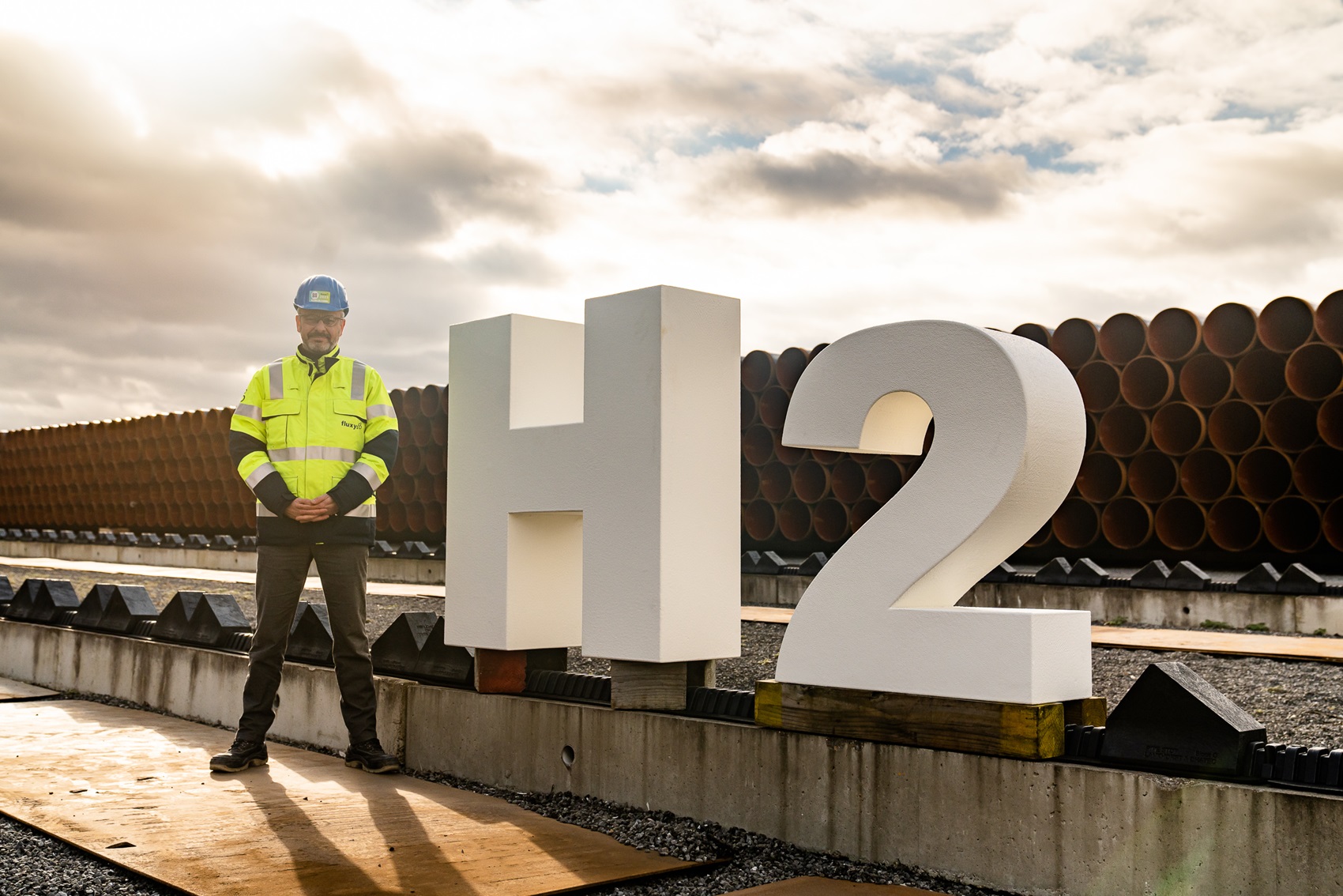Man standing next to H2 sign in front of pipelines.